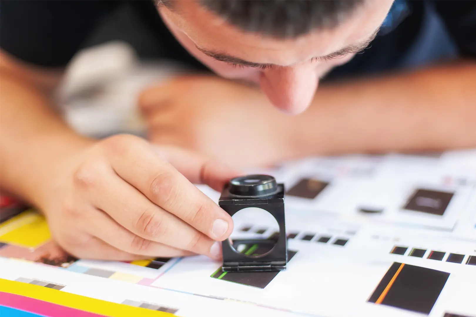 A printing press operator inspecting a printed sheet for colour accuracy